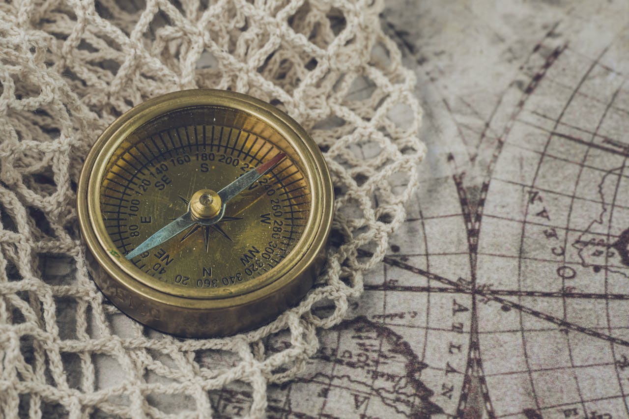 Brass compass resting on an antique world map with crochet details, symbolizing navigation and exploration.